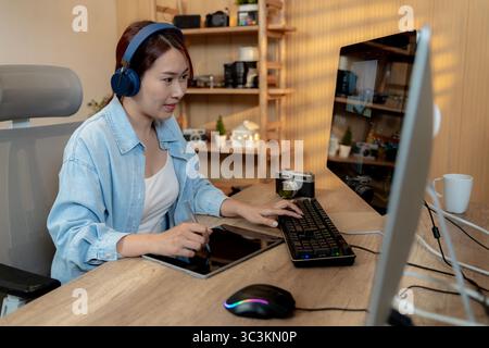 Una giovane e sorridente editor di video freelance che lavora su un notebook a casa, godendosi il suo lavoro creativo in un ambiente rilassato. Foto Stock