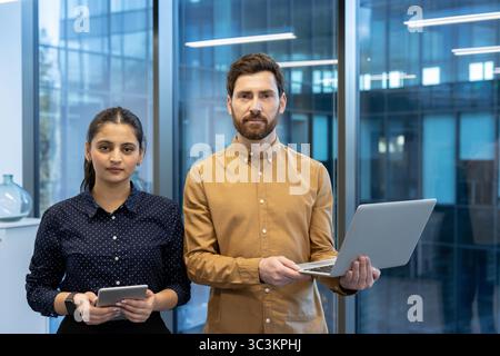 Un team aziendale eterogeneo si pone con fiducia in un ufficio moderno, mostrando lavoro di squadra e professionalità. Foto Stock