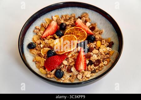Una variopinta ciotola di nutrienti Granola condita con frutta fresca, fette di agrumi secchi e frutti di bosco per una sana colazione. Foto Stock