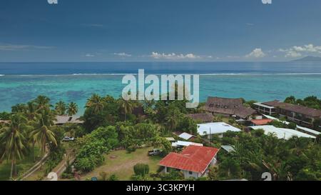 Splendida vista aerea che cattura l'idilliaco paesaggio di Tahiti con acque turchesi, vivaci barriere coralline, vegetazione lussureggiante e case tradizionali lungo la costa Foto Stock