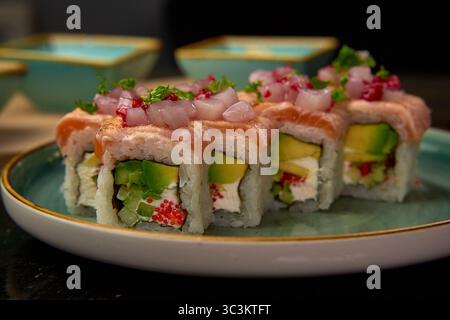 Sushi roll preparato ad arte con salmone, avocado, formaggio spalmabile e guarnito con pezzi di cipolla su un piatto elegante, ideale per una cucina esigente Foto Stock