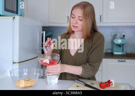 Cucina a casa, donna che prepara il dolce parfait di fragole in una ciotola di vetro. Foto Stock