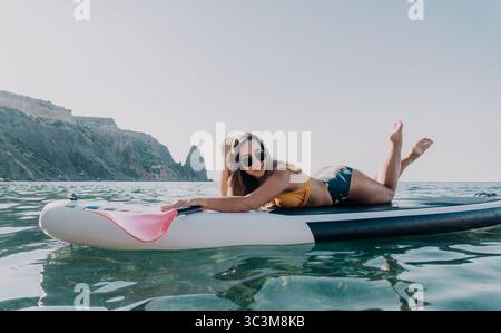Donna Paddleboard Ocean - donna felice sdraiata sul paddleboard nell'oceano con pagaia in mano. Foto Stock