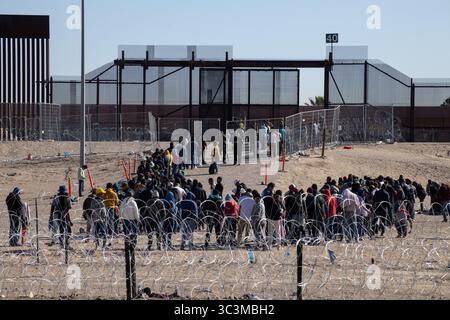 I migranti si radunano al confine di Ciudad Juarez, supervisionati dalle guardie in mezzo a recinzioni spianate. Foto Stock
