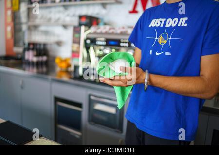 Cremona, Italia - 25 luglio 2025 macchina per il caffè Barista pulizia bacchetta a vapore con panno verde in microfibra per l'igiene e il servizio di qualità presso la caffetteria. Foto Stock