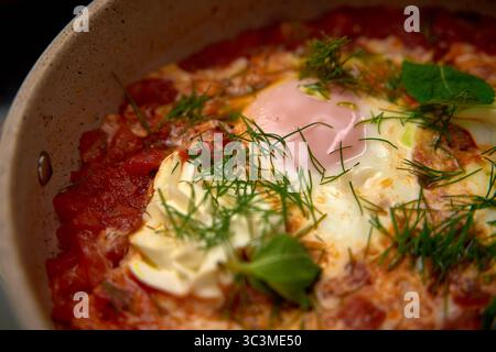 Primo piano di un piatto delizioso e saporito con uova cotte in una ricca salsa di pomodoro condita con erbe fresche e ingredienti cremosi Foto Stock