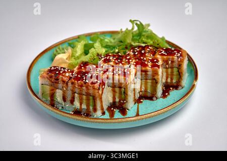 Sushi Rolls preparati con gusto e conditi con salsa dolce e sesamo su un vivace piatto blu con verdure fresche per un'esperienza culinaria squisita Foto Stock