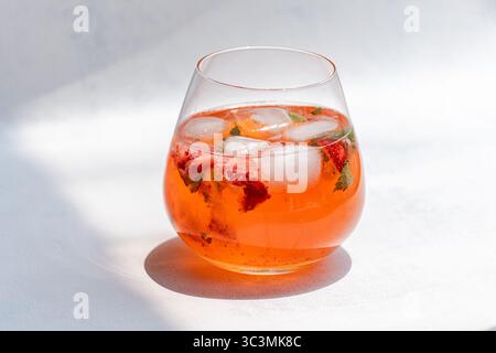 Una vivace e colorata bevanda estiva con fragole fresche, foglie di menta e cubetti di ghiaccio in un bicchiere trasparente, perfetta per rinfrescarsi in una giornata calda. Foto Stock