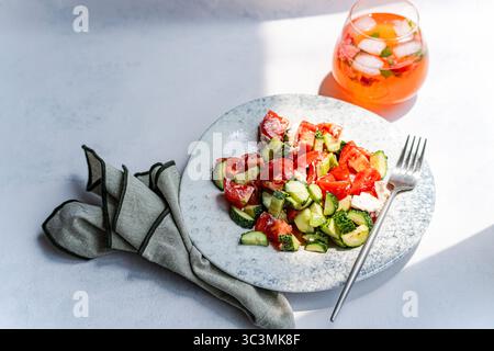 Una vivace insalata estiva con cetrioli freschi, pomodori maturi e formaggio sbriciolato. Questo piatto sano è completato da un rinfrescante fragola dri Foto Stock