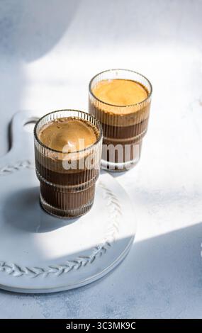 Due bicchieri di cappuccino freddo e frizzante poggiano su un elegante piatto di ceramica bianca, bagnato dalla luce soffusa del sole. La bevanda rinfrescante è perfetta per un caffè Foto Stock
