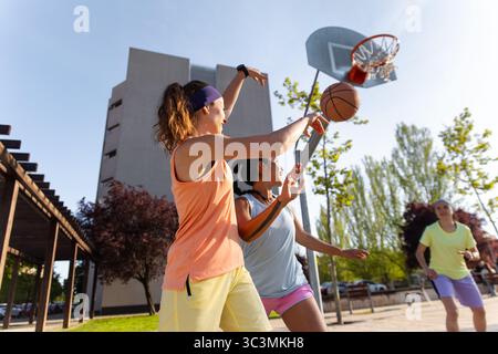 Un gruppo di donne che giocano energicamente a basket in strada su un campo all'aperto. La loro attenzione e il loro lavoro di squadra mettono in risalto l'essenza di Dynamic and compet Foto Stock