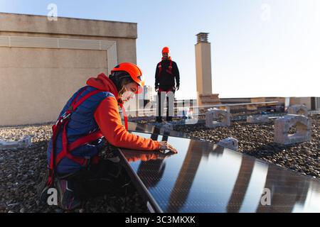 I tecnici degli attrezzi di sicurezza lavorano all'installazione di pannelli solari sul tetto di un edificio, ottimizzando la struttura per una cattura efficiente dell'energia solare Foto Stock