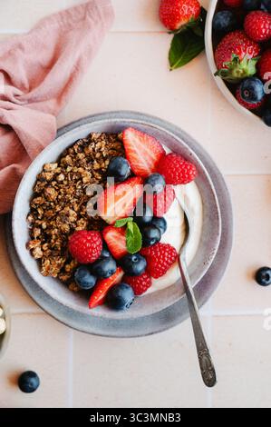Un primo piano di deliziosi granola con fragole, lamponi e mirtilli in una ciotola di ceramica. Una colazione sana e perfetta Foto Stock