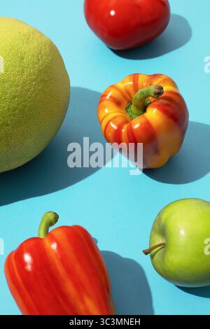 Frutta e verdura in stile pop art dai colori vivaci su una superficie blu che mostra peperoni rossi vivaci, mela verde e pepe d'arancia, creando un vibran Foto Stock