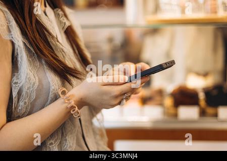 Una donna in un accogliente bar guarda attentamente lo schermo del suo smartphone, magari leggendo o scrivendo messaggi, creando un'atmosfera rilassata e concentrata in mezzo al caffè Foto Stock