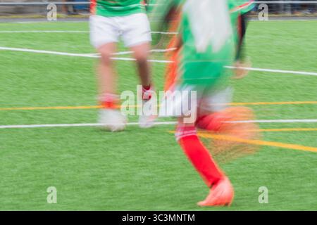 I giocatori di calcio corti e irriconoscibili con maglie verdi, pantaloncini rossi e calze, su un vivace campo di erba verde, creano un'atmosfera dinamica, anonima e senza volto Foto Stock