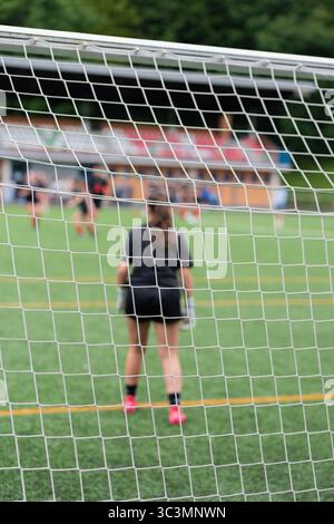 Schiena la vista irriconoscibile di una portiere anonima di calcio di colore nero, in piedi accanto a una rete su un campo di erba verde, pronta a giocare Foto Stock