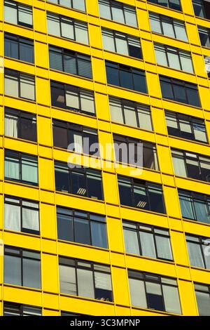 Facciata gialla luminosa di un moderno edificio urbano che presenta un design architettonico contemporaneo. Il pattern ripetitivo della finestra enfatizza le linee geometriche Foto Stock