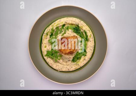 Un piatto splendidamente placcato con pesce scottato su una mousseline cremosa e guarnito con rucola fresca per un'elegante presentazione culinaria Foto Stock