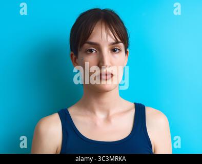 Un ritratto ravvicinato di una donna dall'espressione calma, posto su uno sfondo blu vivace in studio. Indossa un top senza maniche, creando un effetto sorprendente Foto Stock