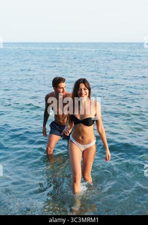 Una giovane coppia gioiosa viene catturata godendosi una giornata di sole sulla spiaggia, nuotando tra le onde cristalline dell'oceano e godendosi compagnia in una foto Foto Stock