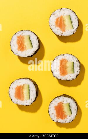 Foto in studio dall'alto di cinque sushi roll con salmone e cetriolo freschi su un vivace sfondo giallo, che presenta un'appetitosa esposizione di giapponesi Foto Stock