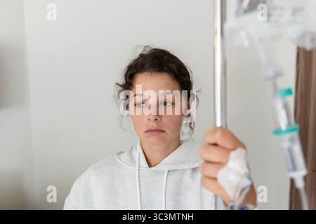 Una giovane donna sta riposando in un letto d'ospedale a Bali, aggrappandosi su un supporto IV. Sembra malata e stanca, circondata dall'ambiente sterile della Foto Stock