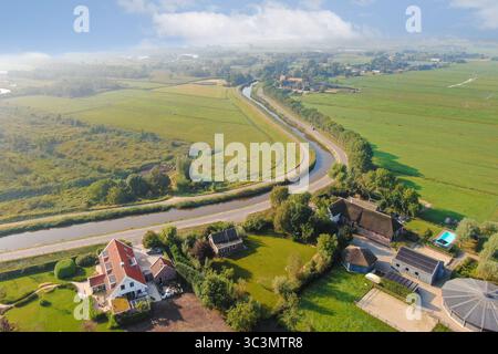 Prospettiva aerea mozzafiato che mostra campi lussureggianti, tortuosi corsi d'acqua e affascinanti case rurali annidate nella tranquilla campagna Foto Stock