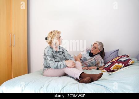 Due amiche anziane si rilassano a casa, condividendo un momento confortevole sul letto. Si godono la compagnia reciproca, evidenziando l'amicizia e il camarad Foto Stock