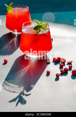 Il vivace e freddo tè estivo a base di fragole e ibisco è guarnito con menta fresca. La rinfrescante bevanda rossa è illuminata dalla luce diretta del sole Foto Stock