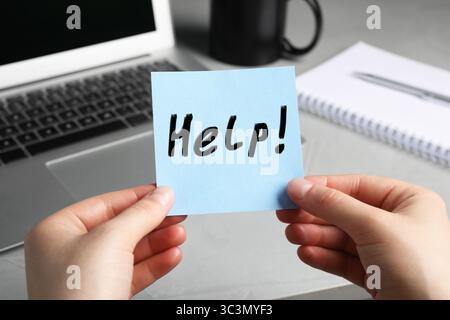 Donna che tiene un biglietto di carta con un aiuto di parole sul posto di lavoro, primo piano Foto Stock