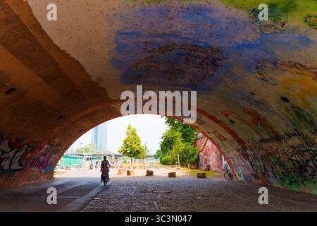 Francoforte, Germania - 10 giugno 2025: Vivace arco coperto di murales con un ciclista che passa in un paesaggio urbano. Foto Stock