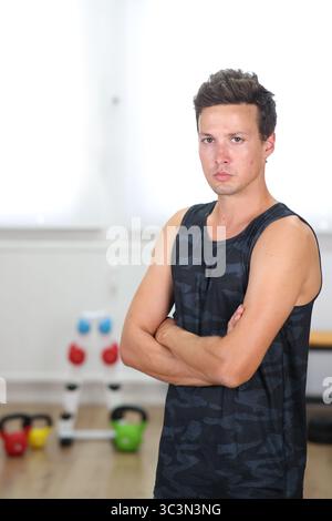 giovane nel centro fitness, braccia incrociate, look poderoso, sfondo chiaro Foto Stock