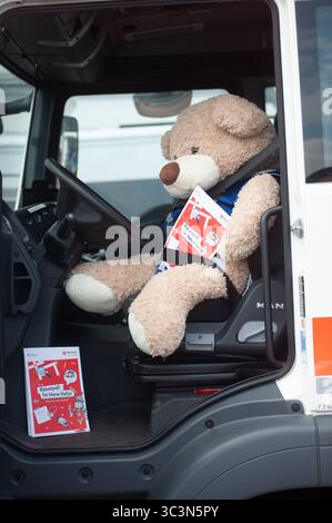 Flensburg, Schleswig-Holstein Flensburger Blaulichttag. DAS Bild zeigt ein sehr Großes Stofftier, einen hellbraunen Teddybär, der angeschnallt auf dem Fahrersitz eines LKW sitzt. Der Teddybär hält ein Heft mit rotem Titelblatt in den Pfoten, auf dem Rätselspaß für kleine Helfer steht. Die Fahrertür des Lkws steht offen, das Innere des Fahrerhauses ist gut sichtbar. Auf dem Trittbrett vor dem Sitz liegt ein weiteres Exemplar des gleichen Hefts. Die Szene wirkt humorvoll und kindgerecht, und macht im Rahmen der Information- und Kinderaktion, auf Verkehrssicherheit und das Thema Toter Winkel auf Foto Stock