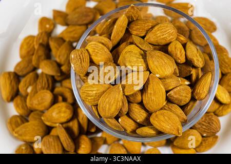 Ciotola di mandorle arrostite su una superficie bianca con vista ravvicinata Foto Stock