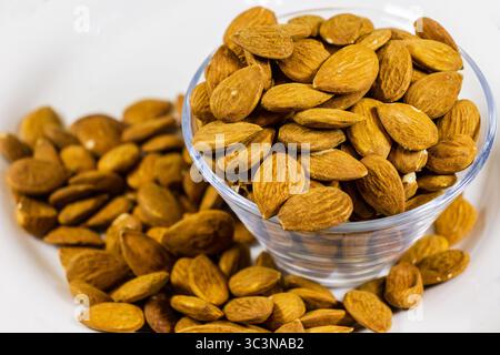 Deliziose mandorle in una ciotola di vetro circondata da dadi sparsi Foto Stock