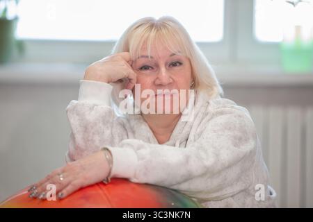 Una donna matura siede comodamente con il mento appoggiato sulla mano, sorridendo dolcemente mentre si appoggia contro un globo colorato. La sala luminosa dispone di wi-fi Foto Stock