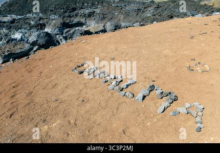 Roccia lavica che scrive «la Palma» su un altopiano sabbioso di scogliera, con formazioni vulcaniche al largo di la Palma sullo sfondo. Foto Stock