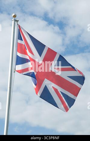 La bandiera Union Jack sventola orgogliosamente su un palo sotto un cielo blu pieno di nuvole bianche, mostrando una giornata vibrante e limpida. Foto Stock