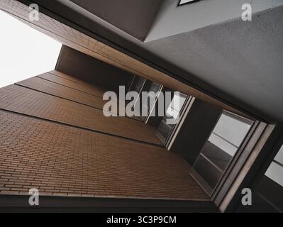 Stretta vista prospettica della facciata di un edificio residenziale che mette in risalto le pareti in mattoni arancioni. I pattern verticali delle finestre rettangolari sono intervallati Foto Stock