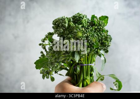 Vista di una mano che regge un fascio di broccolini. Foto Stock