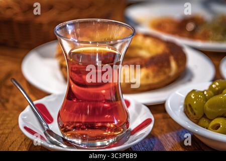 Tradizionale bicchiere di tè turco o chai a forma di tulipano servito in un bicchiere di tulipano con simit e olive in un ristorante per colazione, Istanbul, Turchia Foto Stock