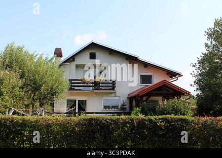 Una casa bianca contemporanea a due piani presenta un prominente balcone frontale con gerani in fiore pelargonium, un porto coperto e grandi finestre Foto Stock