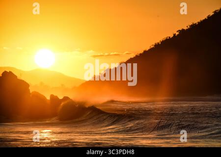 Ultima luce Misty Sun Rays of a Crimson Sunset. Schiuma spray Waves Rise Roll Crash Break Foto Stock