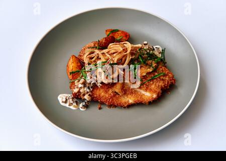 Cotoletta di pollo impanata croccante servita su un piatto elegante con verdure saltate, guarnita con erbe fresche e salsa cremosa Foto Stock