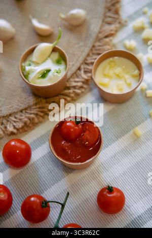 Un assortimento di ingredienti freschi, tra cui pomodori ciliegini, salse e aglio, preparati su una tovaglia testurizzata per una delizia culinaria Foto Stock