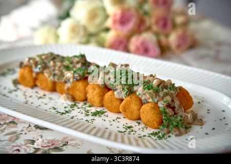 Delizioso piatto con crocchette d'oro condite con crema di funghi e erbe verdi fresche placcate elegantemente per una delizia culinaria Foto Stock