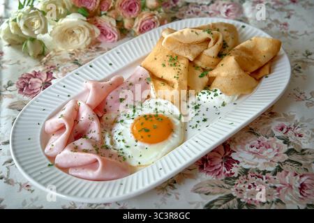 Un delizioso piatto con uova fritte, prosciutto salato e frittelle dorate adornate con erbe fresche, perfetto per una deliziosa colazione Foto Stock