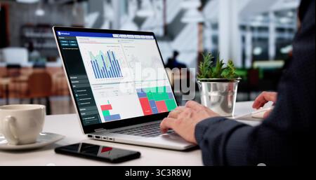 Uomo d'affari che analizza i grafici dei dati su un notebook in Cafe Foto Stock