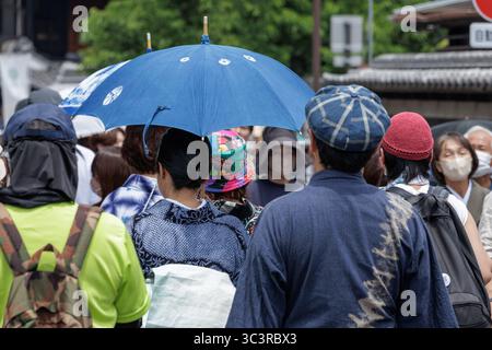 Un importante ombrello blu si distingue tra una folla variegata di frequentatori dell'Arimatsu Shibori Festival. Abbigliamento estivo tie-dyed dots Crowd, Nagoya, Giappone, 7 giugno 2025. Foto Stock